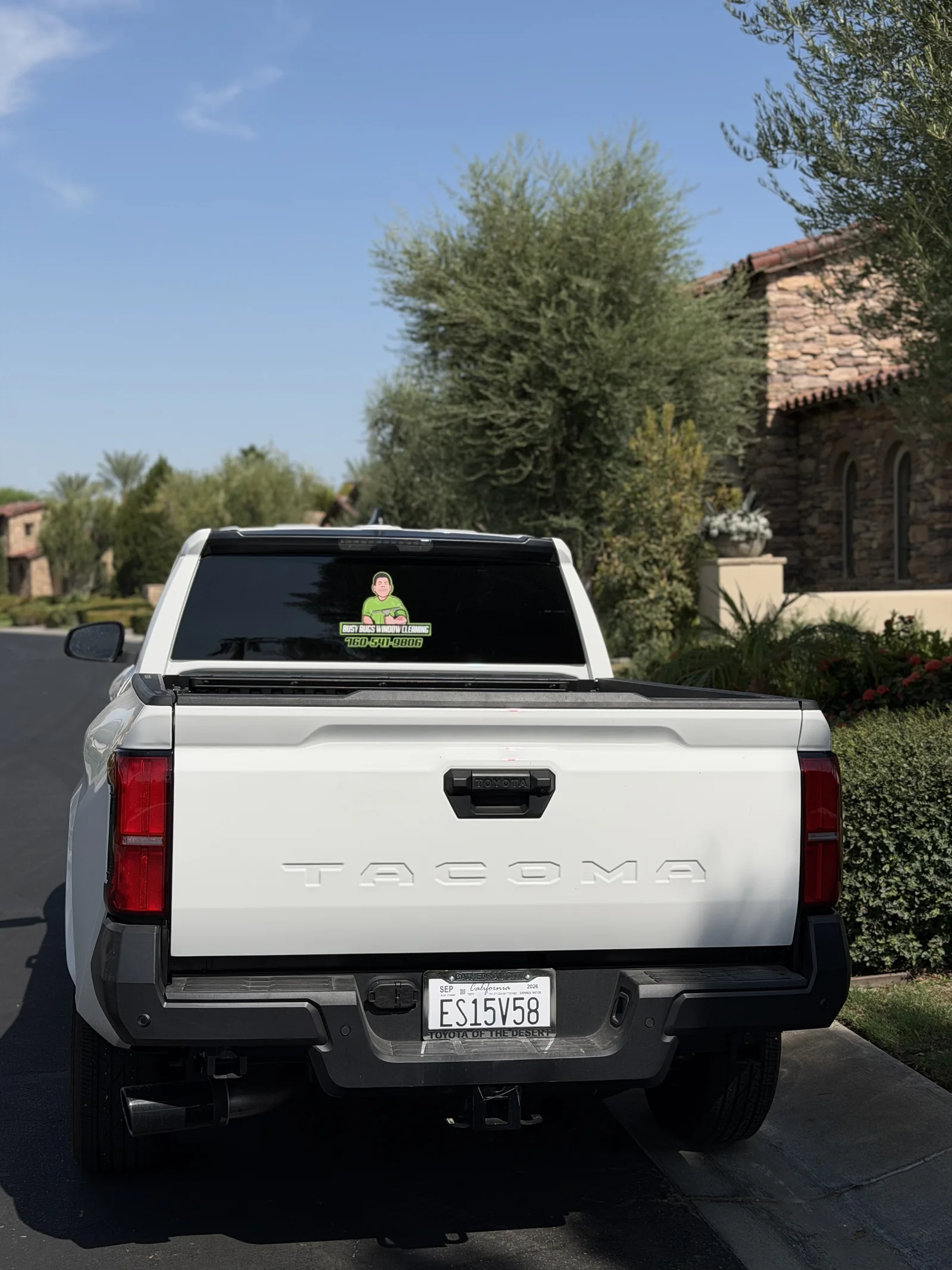 Rear view of the white 2026 Toyota Tacoma Busy Bugs work truck with branded rear window at a Toscana Country Club residence in Indian Wells