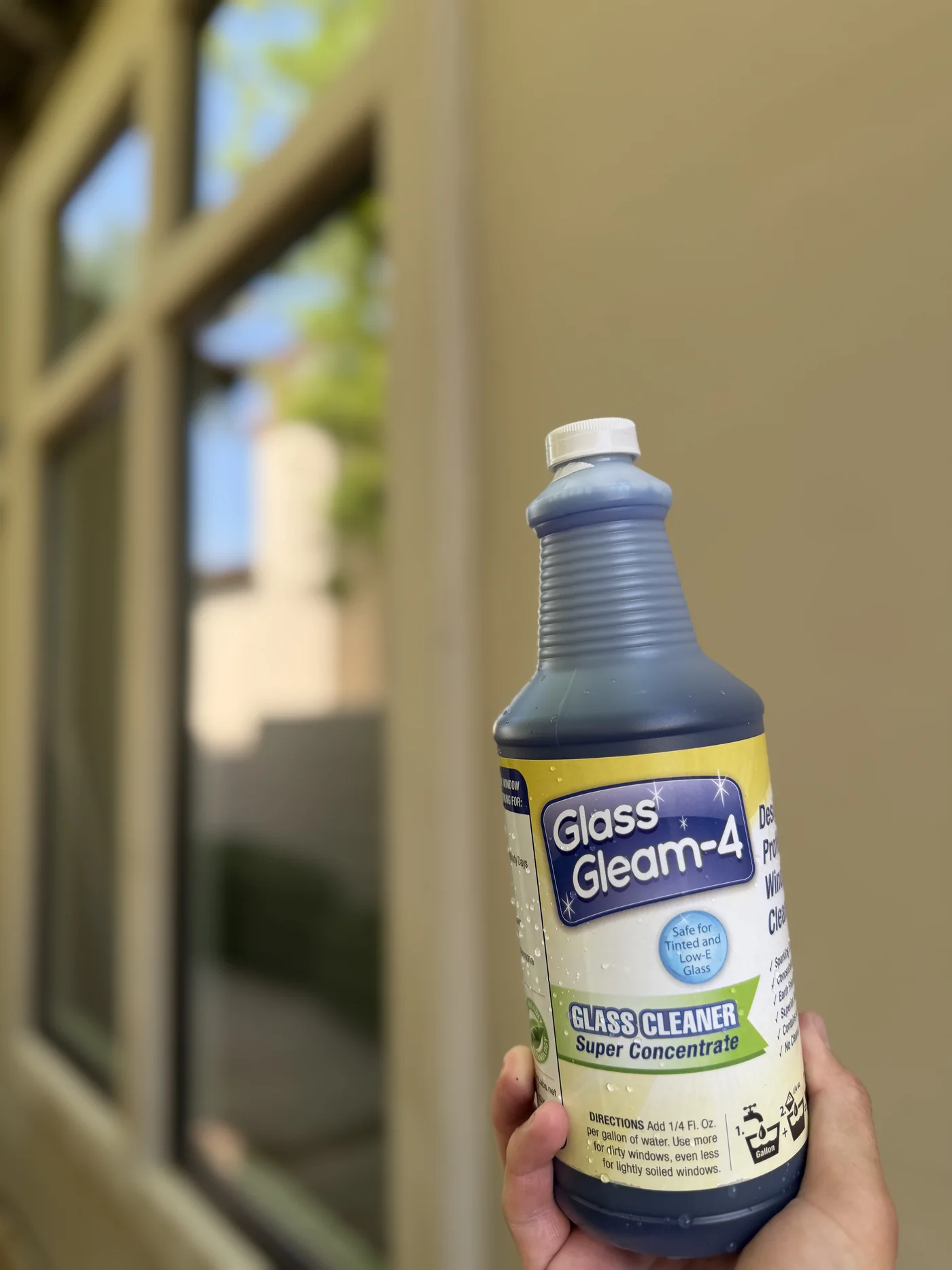 Bottle of Glass Gleam-4 professional glass cleaner held in front of residential windows
