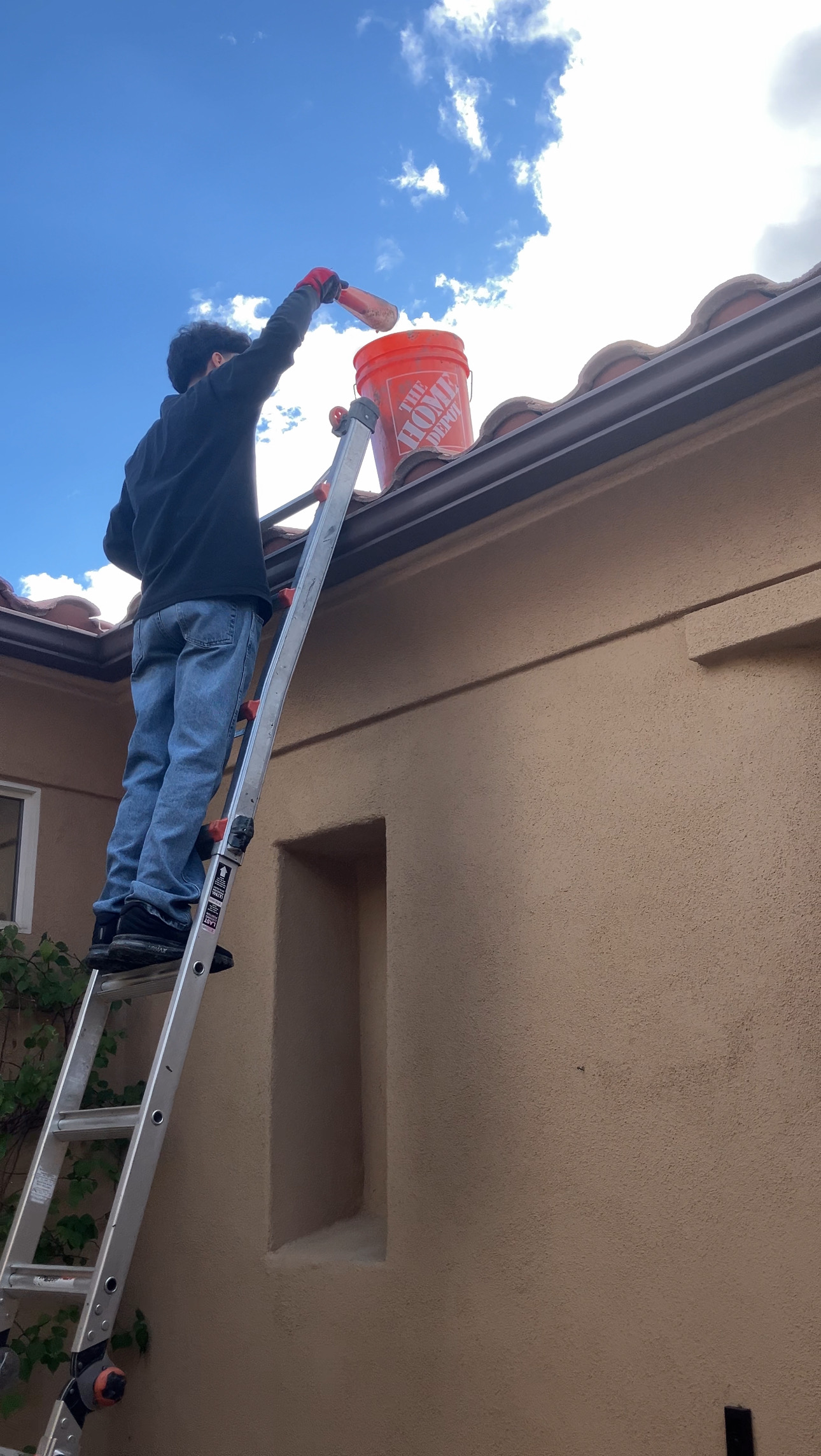 Professional gutter cleaning service in Palm Springs, worker removing leaves and debris from a tile roof gutter.